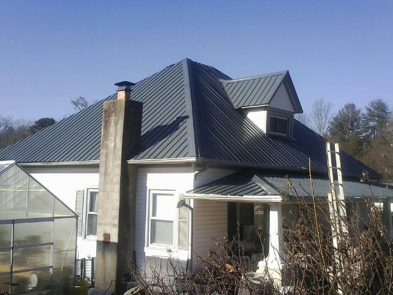 Dark blue standing seam metal roof on a white farmhouse with dormer — Slate & Tile Roof Repair by Roofing Brothers in Prairie View