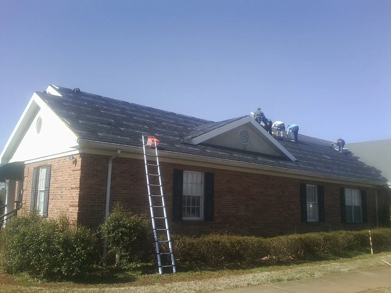 Crew tearing shingles off a brick ranch roof with a ladder set — Metal Roof Repair work by our crew in Prairie View