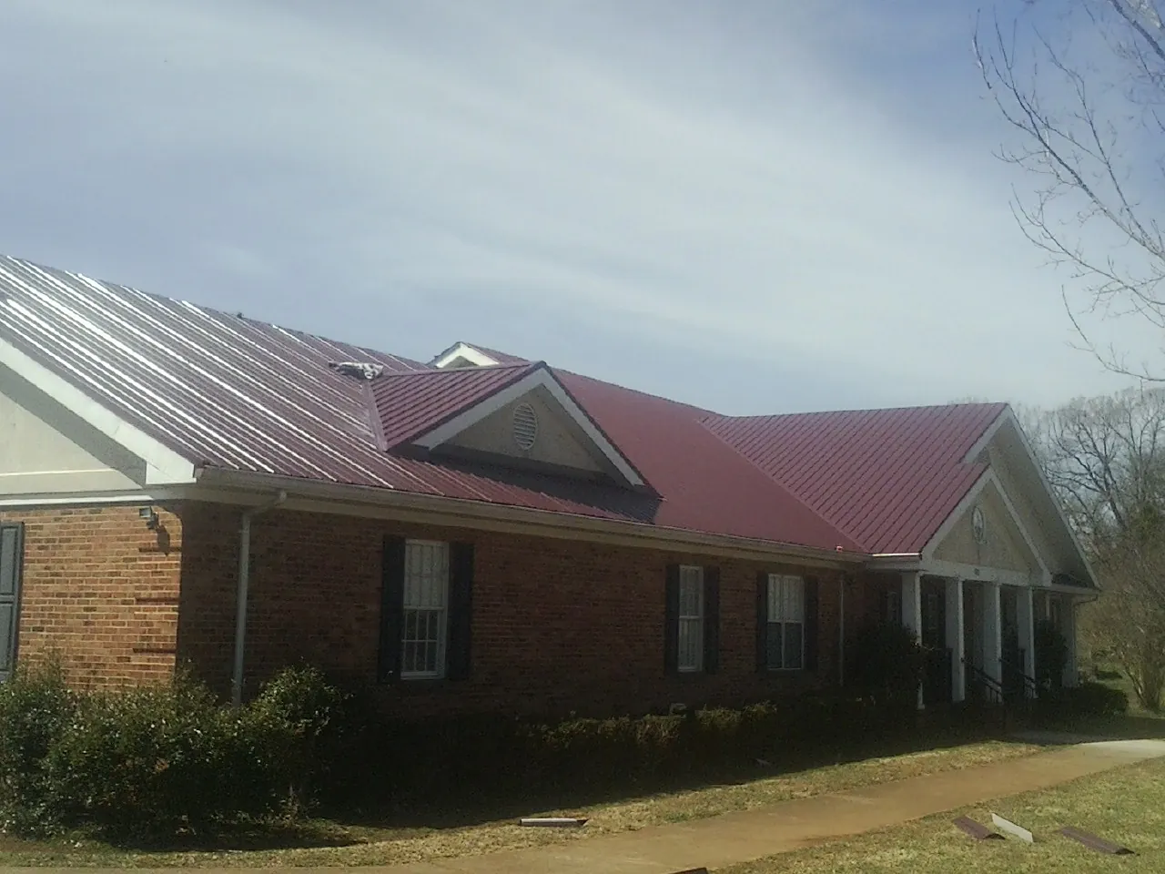 Red metal roof with gabled entries on a long brick building, from a Hail Damage Roof Repair job in Prairie View