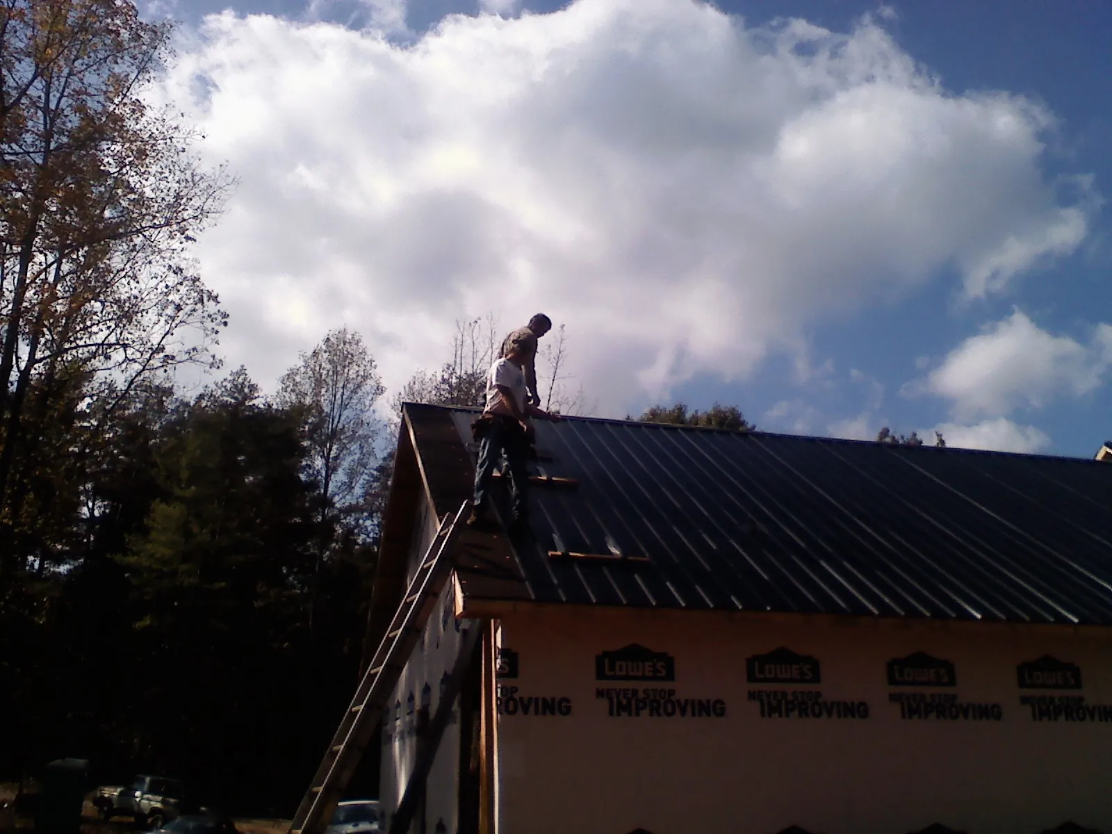 Roofer fastening dark metal panels high against a cloudy sky, from a Roof Inspection job in Prairie View