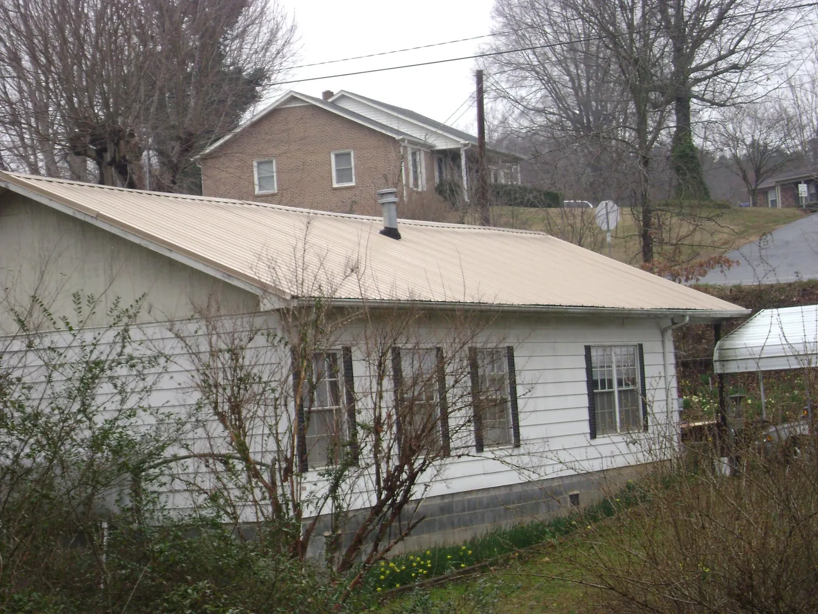 Tan metal roof on a white sided house set into a hillside — Commercial Roofing by Roofing Brothers in Prairie View